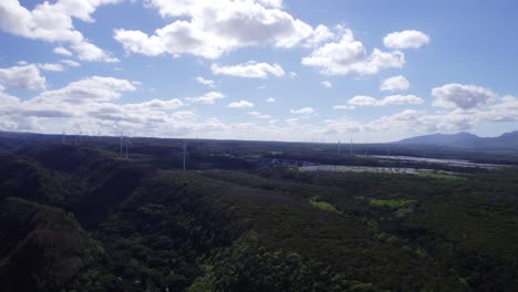 drone-shot-panning-left-of-the-landscape-near-North-Shore-Oahu-Hawaii-showing-the-green-energy-windmills-across-the-mountain-peaks-with-white-puffy-clouds-on-a-sunny-day