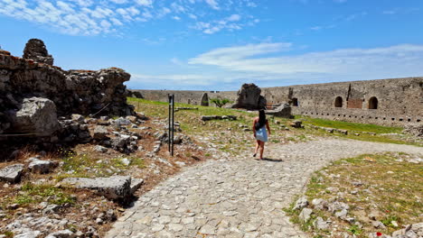 Young-woman-walking-along-a-cobblestone-pathway-towards-a-medieval-castle