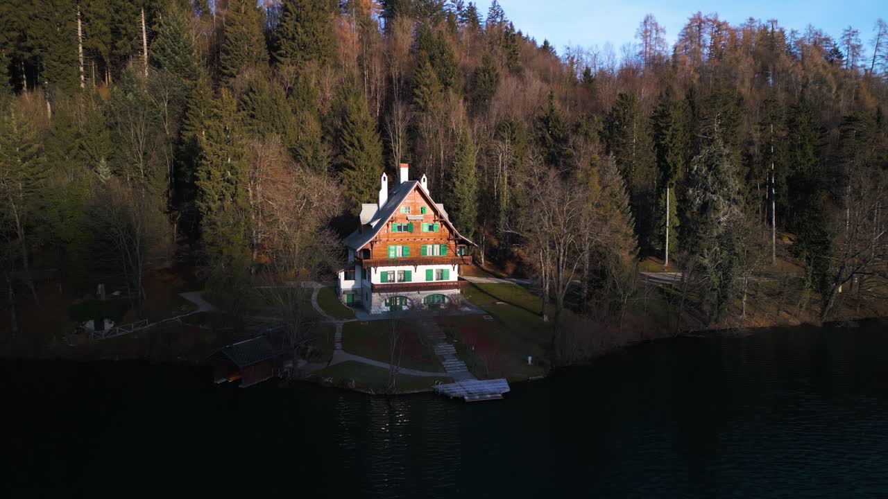 Ripresa aerea in allontanamento con effetto parallasse mostra una bella casa in legno sul lago immersa nella foresta