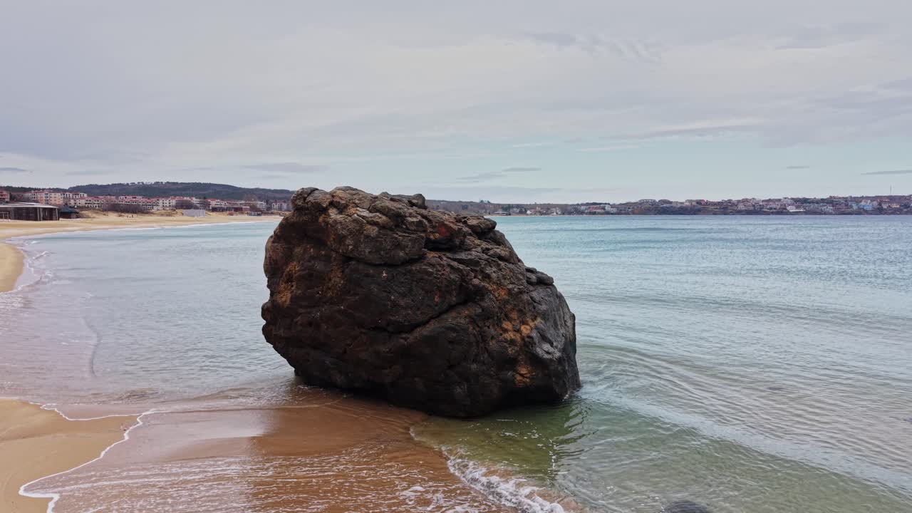 Klippe står på sandstrand nær det rolige hav på en overskyet dag