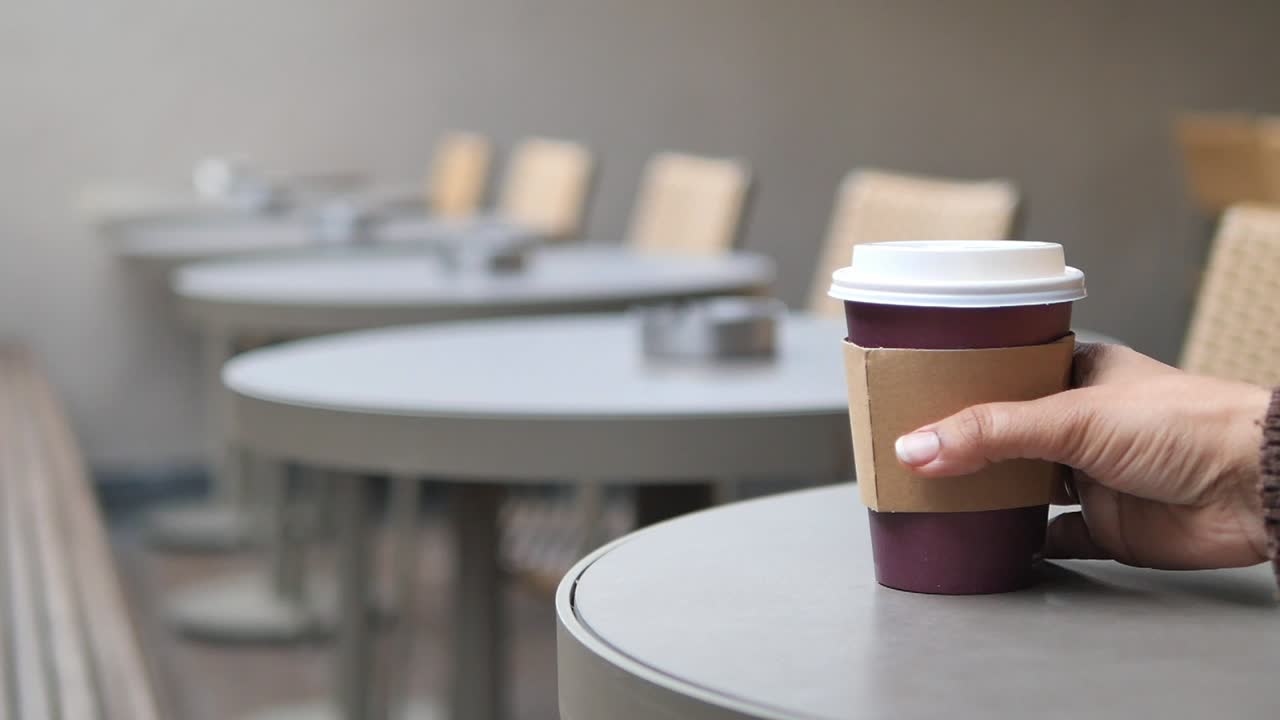 Mano che prende una tazza di caffè usa e getta dal tavolo di un bar.