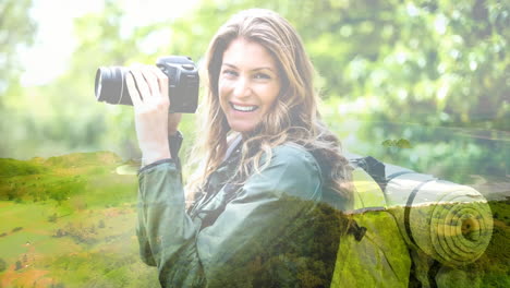 smiling woman holding camera over lush green landscape with hills and trees