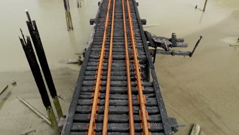 charred railway tracks extend over the muddy riverbed in richmond, british columbia, canada - drone flying forward