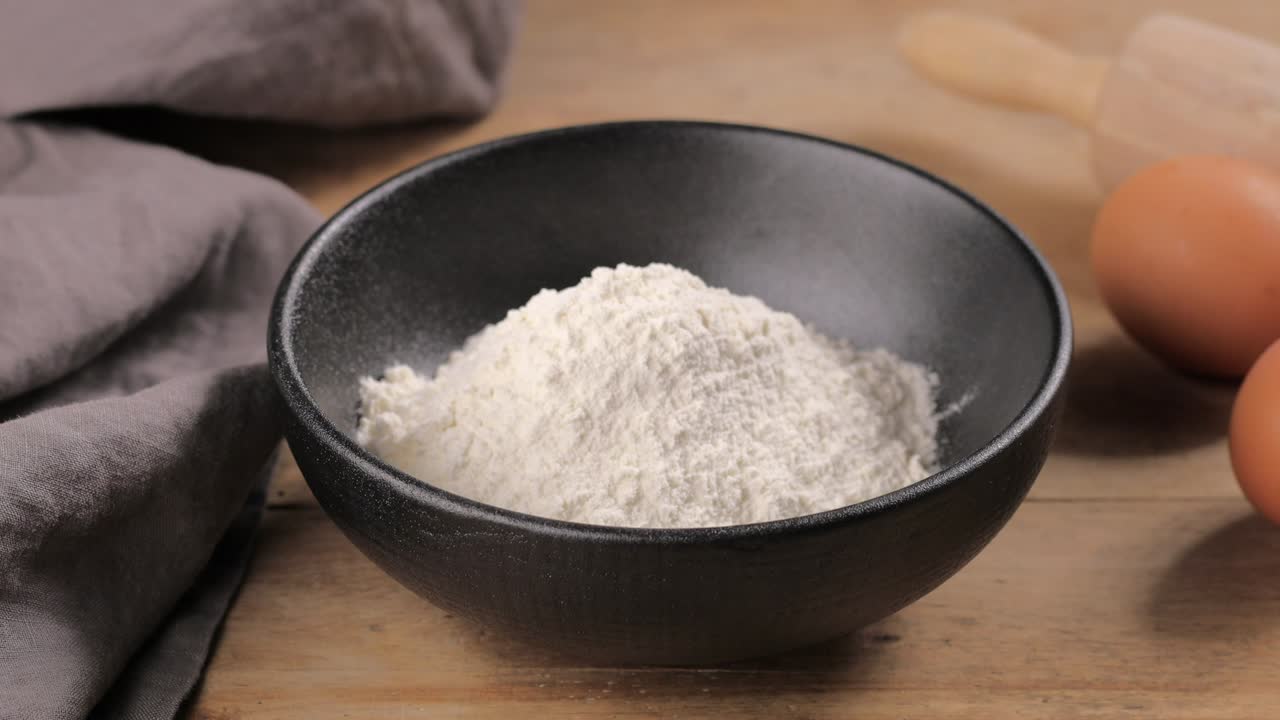 cook puts flour in a bowl with a wooden spoon for making dough