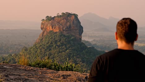 a man gazes thoughtfully at the iconic sigiriya rock as the sun rises over the lush landscape of sri lanka.
