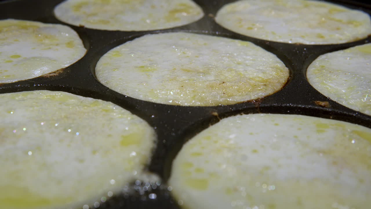 Friggere mini pancake svedesi chiamati plättar, in una padella nera. Concetto di cucina casalinga. Fumo dalla frittura