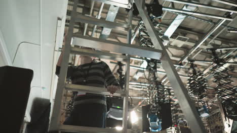 studio technician climbing ladder for equipment adjustment, managing lights, camera setups in broadcast studio, overseeing production environment, preparing for filming in studio space