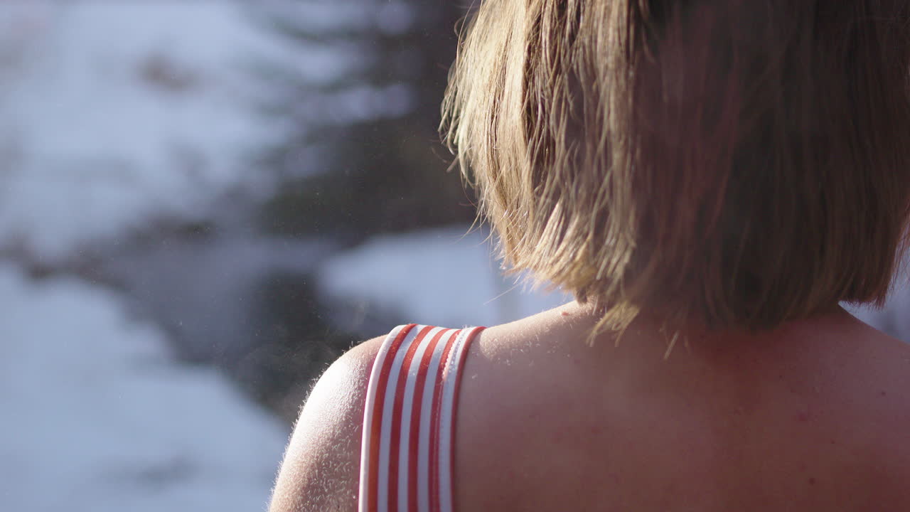 Steaming hot skin of woman stepping out of sauna into snowy outdoors, rear view