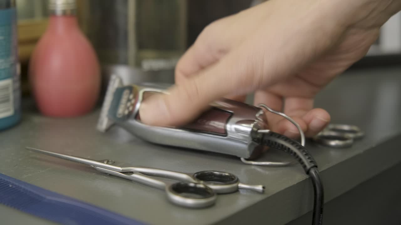 Barber picking up hair trimmer and scissors at barbershop in central London
