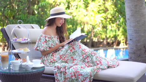 una mujer joven y bonita con un vestido de verano y un sombrero de paja se sienta en un salón de persecución mientras lee su libro