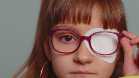 sick ill preteen girl looking at camera, having protective bandage plaster patch scratch on one eye