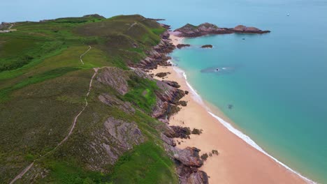 scenic cap d'erquy peninsula with lush green heathland, rocky coast, sandy beach, and turquoise water, brittany, france. aerial drone descending