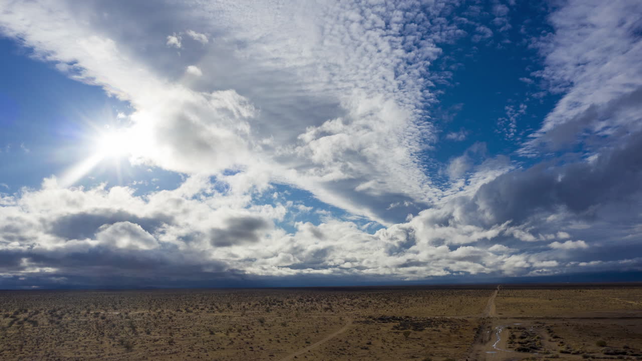 Vast desert landscape under dramatic cloudy sky with sunburst