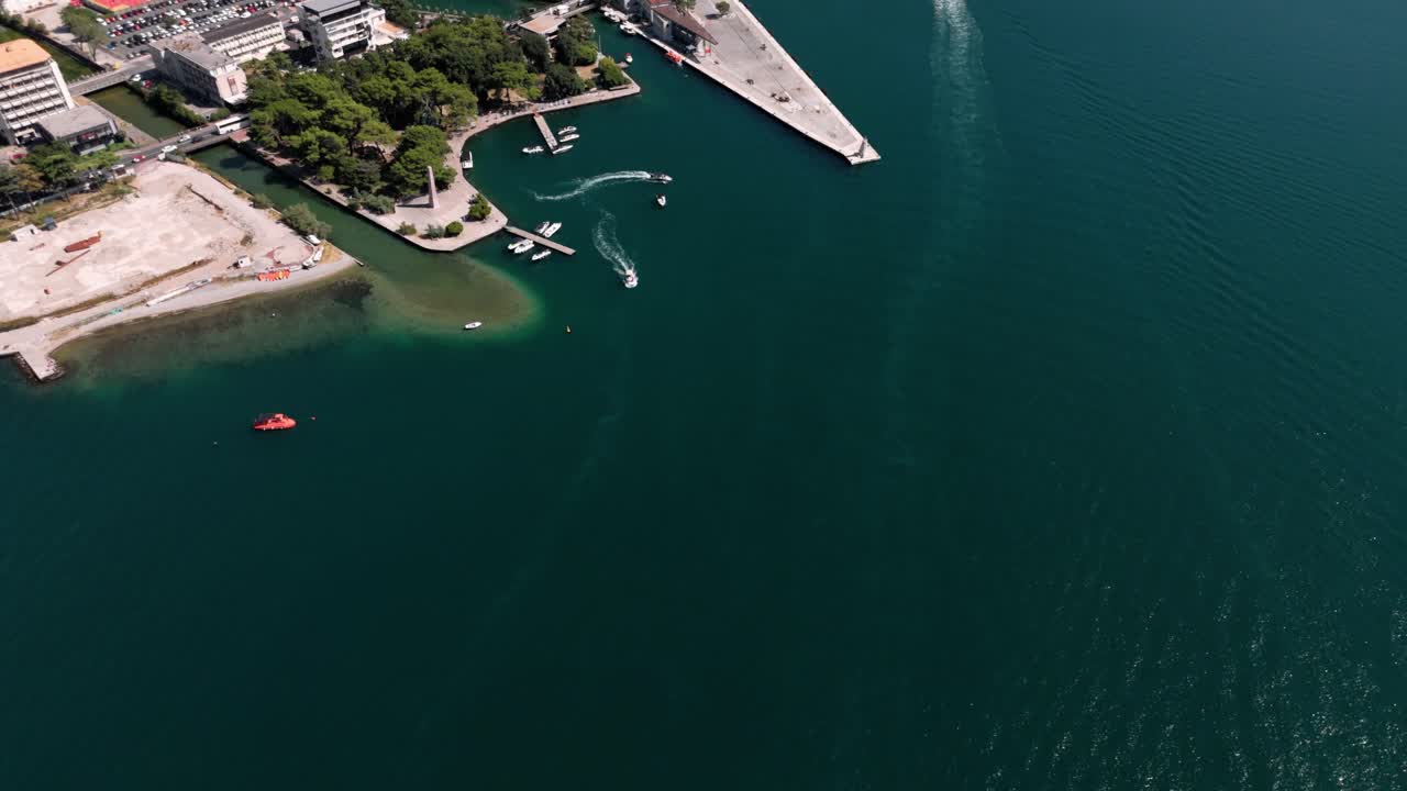 Aerial reveal of the port and fortress of Kotor with its city in front of the hill and beutiful adreatic ocean will a small boat arriving at the sea gate