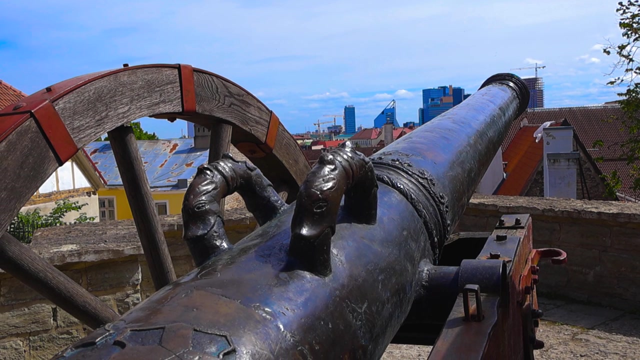 Vecchio cannone medievale Roter Lowe su un muro difensivo puntato verso lo skyline moderno, mostrando il contrasto tra la storica Città Vecchia e la città contemporanea di Tallinn, Estonia