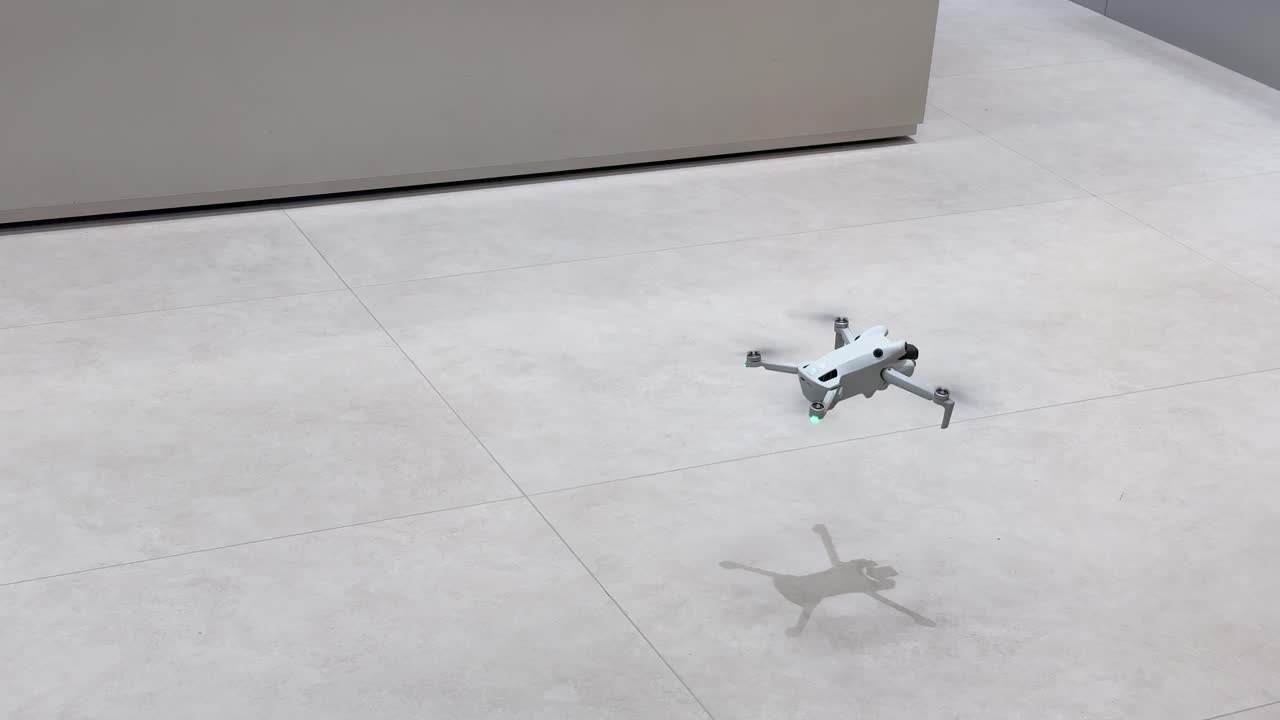 Compact quadcopter hovers and maneuvers in bright, modern indoor workshop with smooth camera tracking