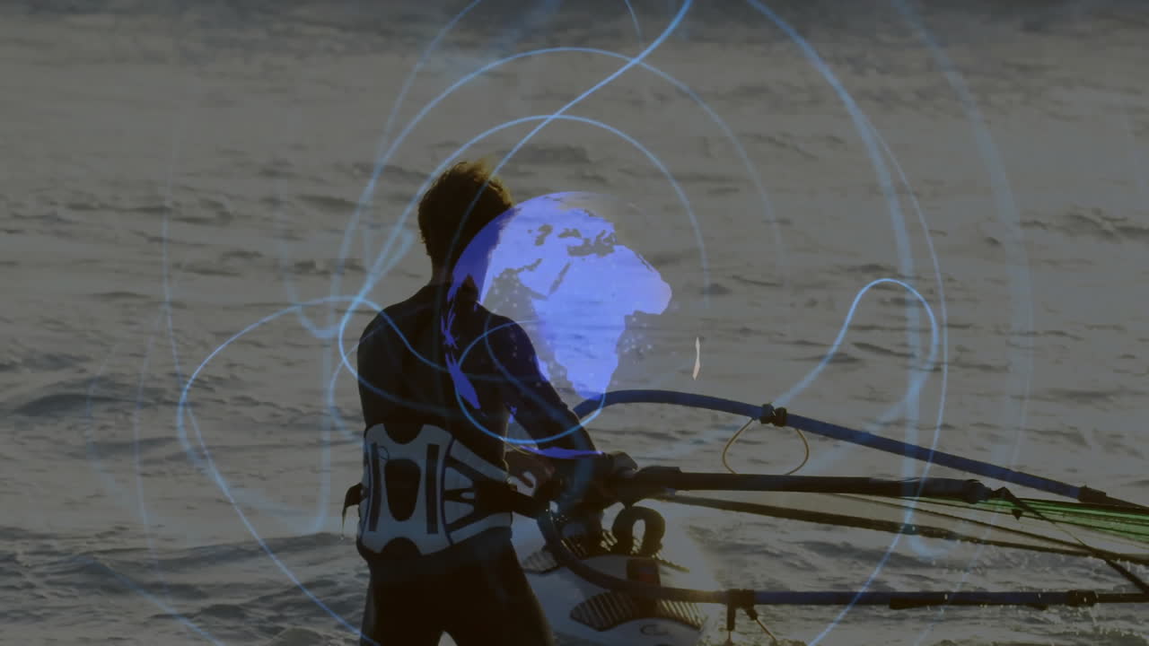 Man adjusting windsurfing sail in shallow ocean water, showcasing digital globe network overlay