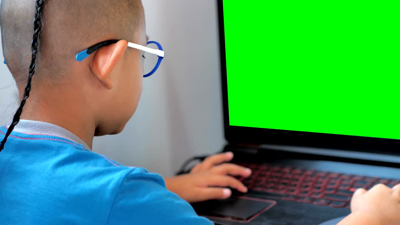 un niño asiático jugando con una computadora portátil y una pantalla verde.
