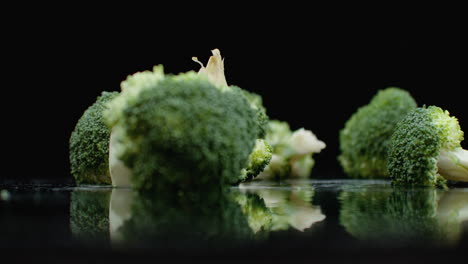 three green fresh broccoli fall on a glass with splashes and drops of water in slow motion on a dark background. ingredients for salad healthy food.