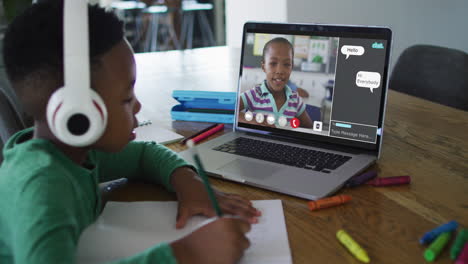 schoolboy using laptop for online lesson at home, with schoolgirl talking and web chat on screen