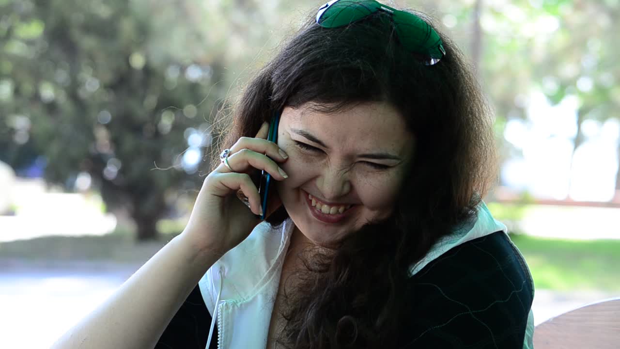 Filmagem na primavera. A jovem e linda garota em uma mesa de café com o celular.