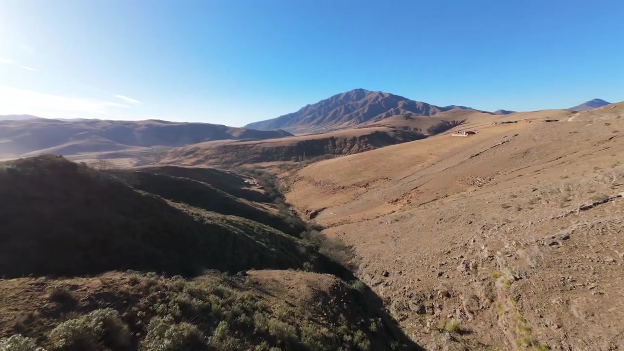 Vista aerea FPV avventurosa di una tortuosa strada sterrata di montagna prima di virare per tuffarsi in un canyon aspro e arido a Tucumán. Durante un pomeriggio sereno.