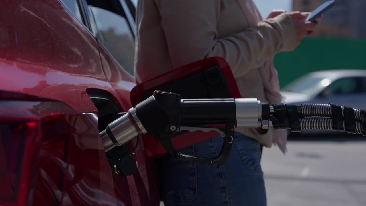 Persona che fa rifornimento a un'auto rossa alla stazione di servizio mentre usa lo smartphone