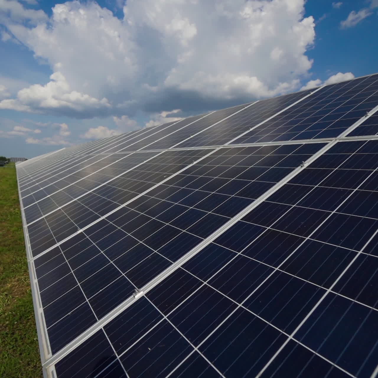 Close-up of solar panel under the cloudy sky. Alternative source of energy. Blue solar cell panel on green grass. Slow motion.