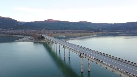 Vorwärtsdrohne-Schoss-Während-Der-Blauen-Stunde-über-Eine-Brücke-An-Einem-See-In-Griechenland