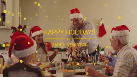 animation of happy holidays and new year text with spots over family in santa hats at dinner table
