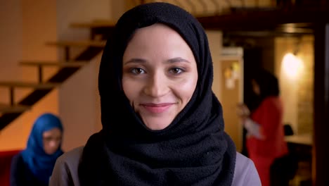 closeup portrait of young beautiful arabian businesswoman in black hijab looking at camera and laughing happily on the workplace indoors