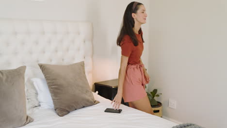 young woman relaxing on bed, using smartphone, enjoying leisure time at home