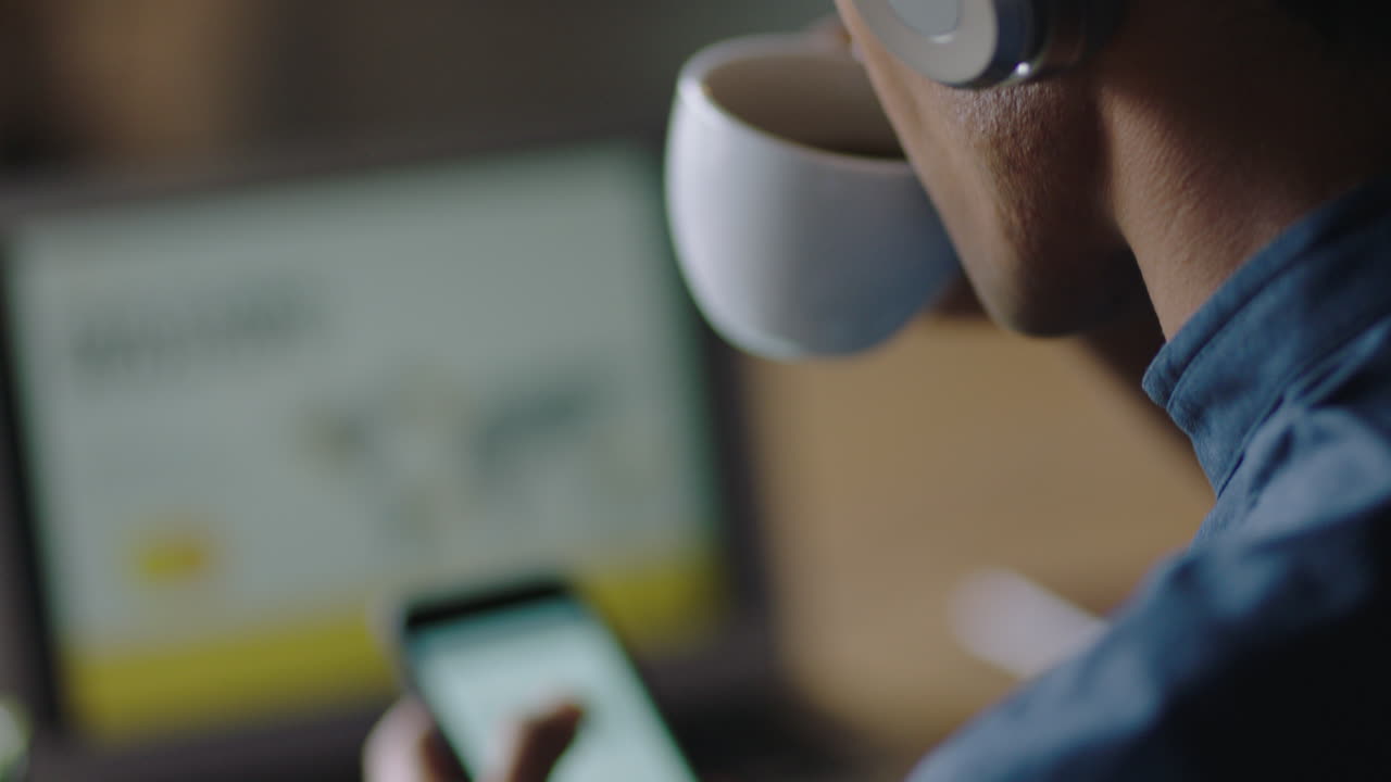 close up giovane uomo d'affari che usa lo smartphone in un caffè che beve caffè che naviga messaggi e-mail che si collega online che invia messaggi di testo che ascolta musica che indossa le cuffie