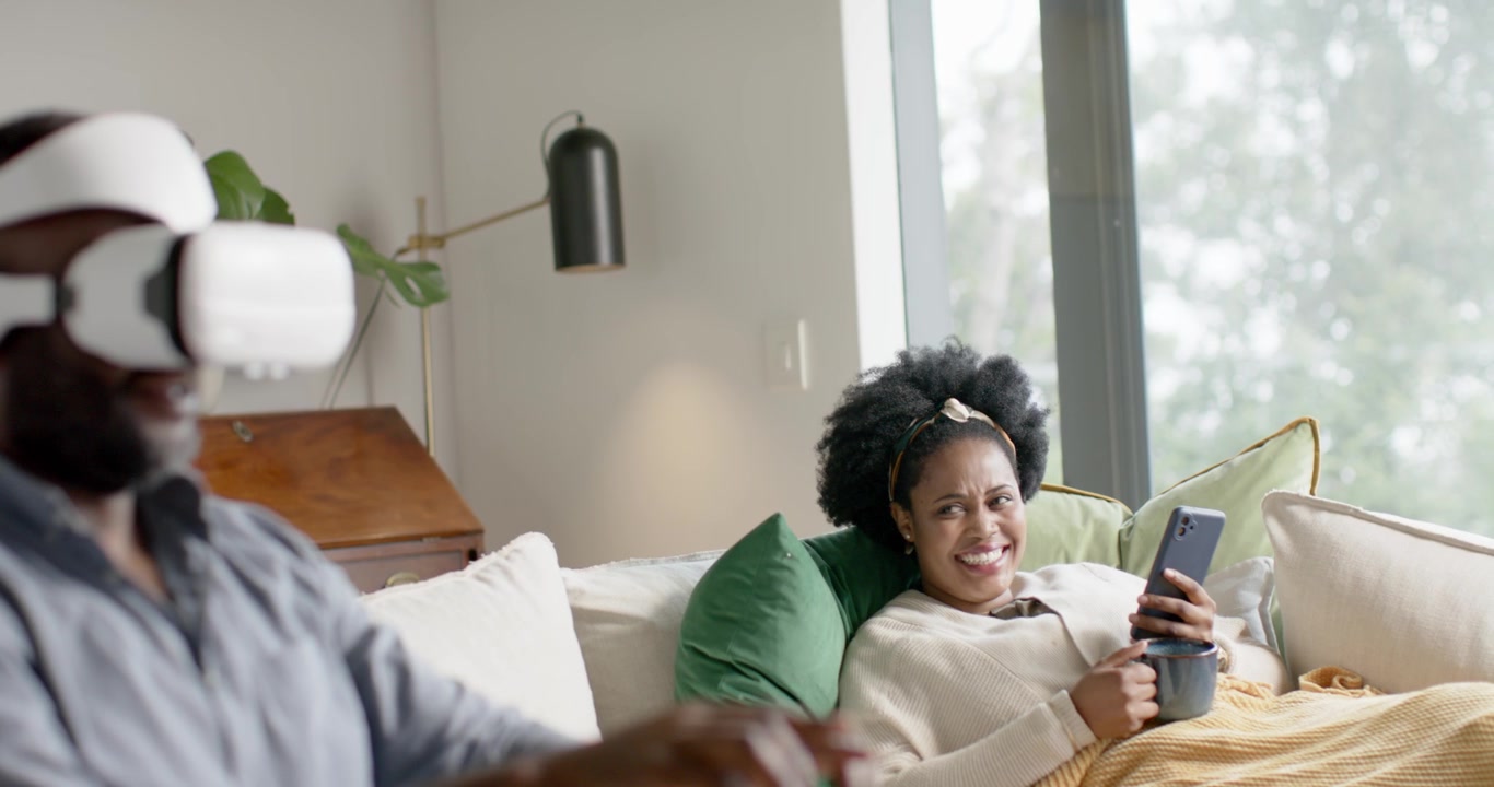 African American couple reacting after VR headset activating, man using headset, woman holding mug