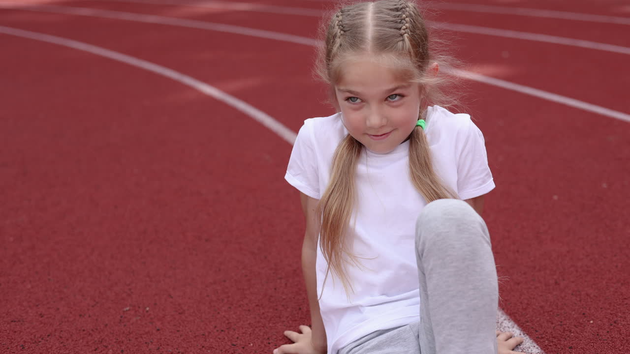 A little girl is doing sports on the sports ground. A child is playing outdoors. A stylish girl in a white T-shirt. A girl with braided hair