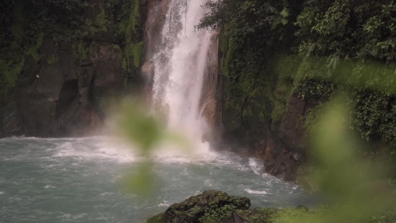 The dense, green rainforest foliage surrounds the scene, highlighting the mystical and ethereal atmosphere of the Rio Celeste waterfall