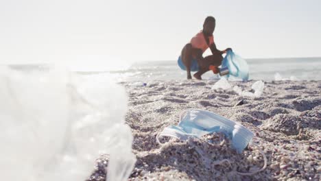 African-american-man-segregating-waste-with-gloves-on-sunny-beach