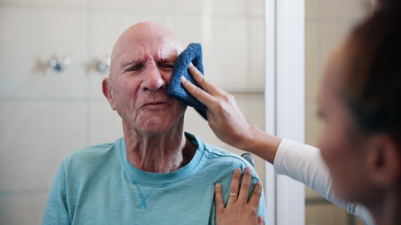 Elderly man receiving assistance from a caregiver with a towel in the bathroom