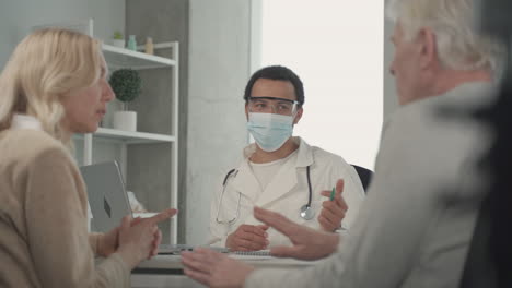 a young black doctor in a facemask talking to a ederly couple 1