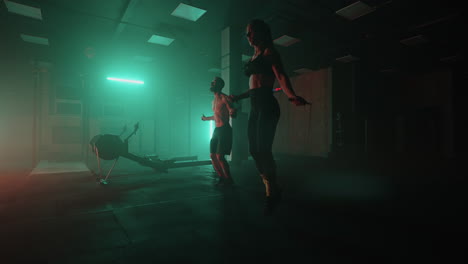 a man and a woman in a colored neon red and blue light in slow motion jump rope together. endurance training. the concept of athletic and strong couples