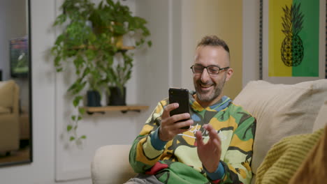 hombre relajándose en el sofá, encuentra diversión en lo que lee en su teléfono inteligente