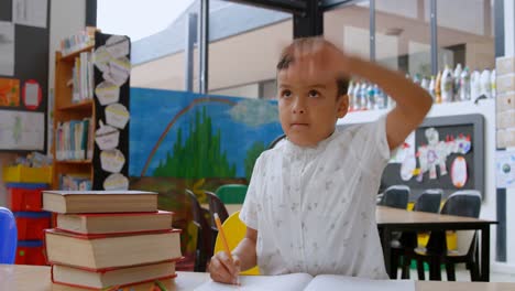 front view of asian schoolboy raising hand while studying on desk in classroom at school 4k