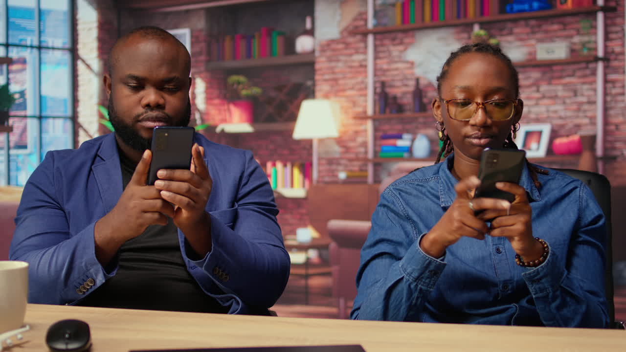 Black couple at home analyzing financial reports on their mobile phones