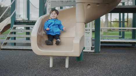 cheerful asian kid descends from the slide on the playground