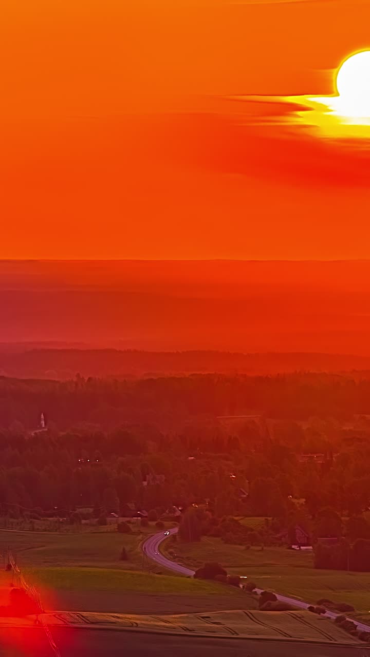 breathtaking aerial view timelapse of massive sun disk descending through orange clouds over curved country highway and lush green valley in latvia