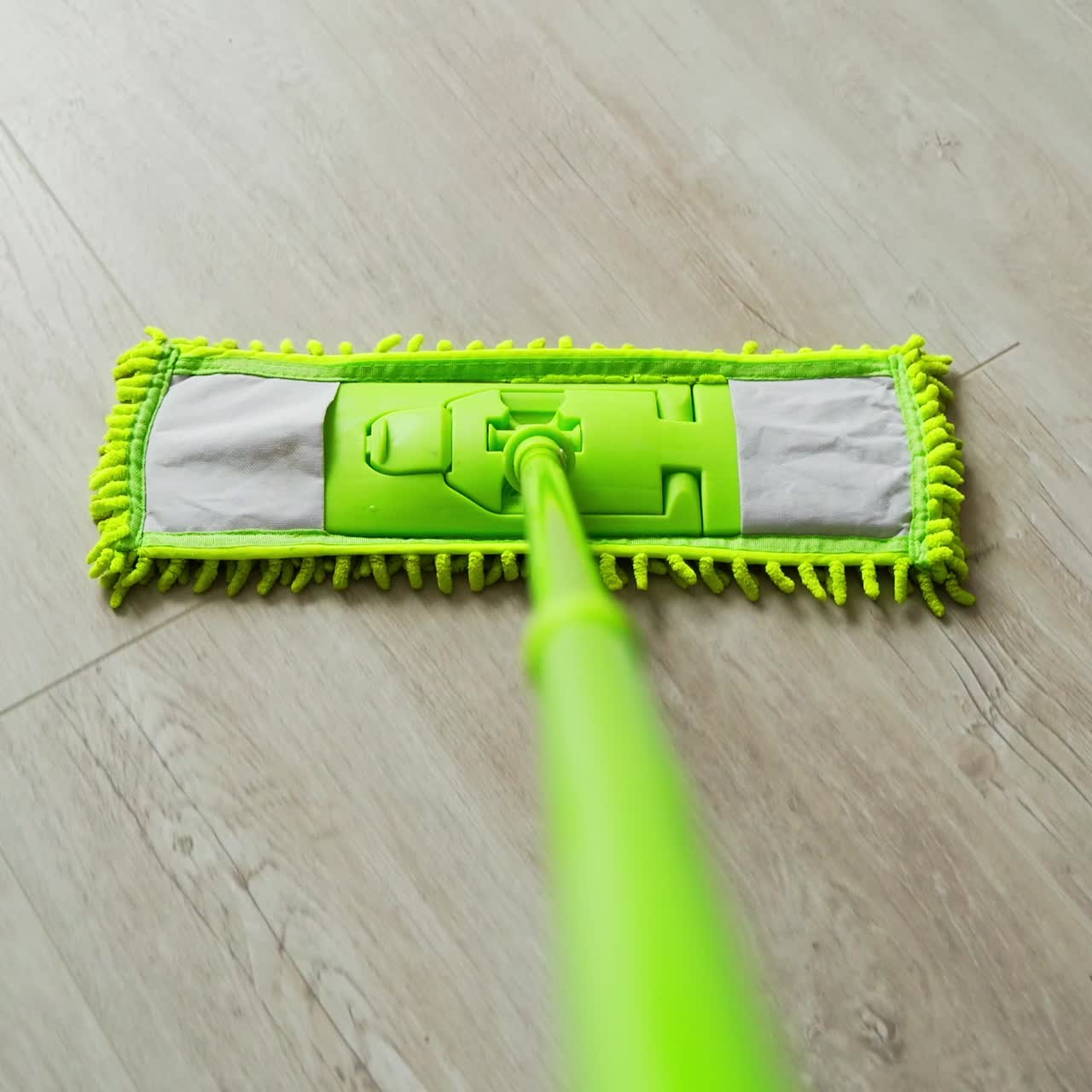 New green mop moving on parquet floor. Cleaning the house with a microfiber mop. Domestic chores. Close-up.