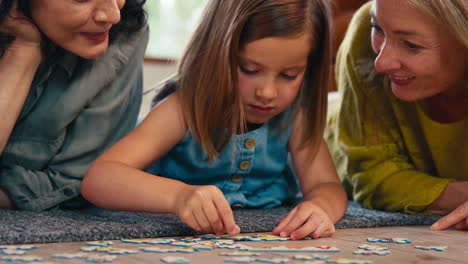 close up of same sex family with two mature mums and daughter lying on floor doing jigsaw puzzle