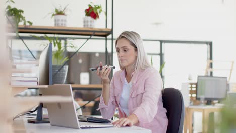 Busy-caucasian-businesswoman-using-laptop-and-talking-on-smartphone-at-table-in-slow-motion