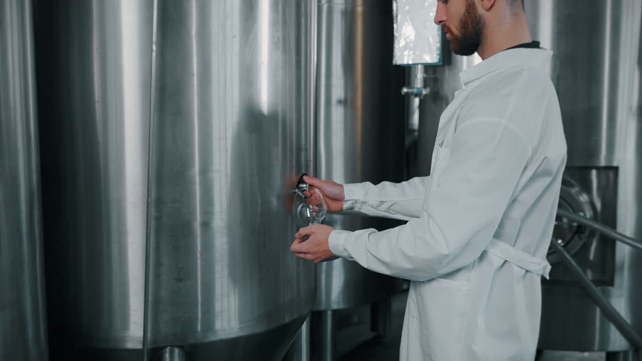 trabajador de una cervecería llenando vidrio en un tanque de acero inoxidable