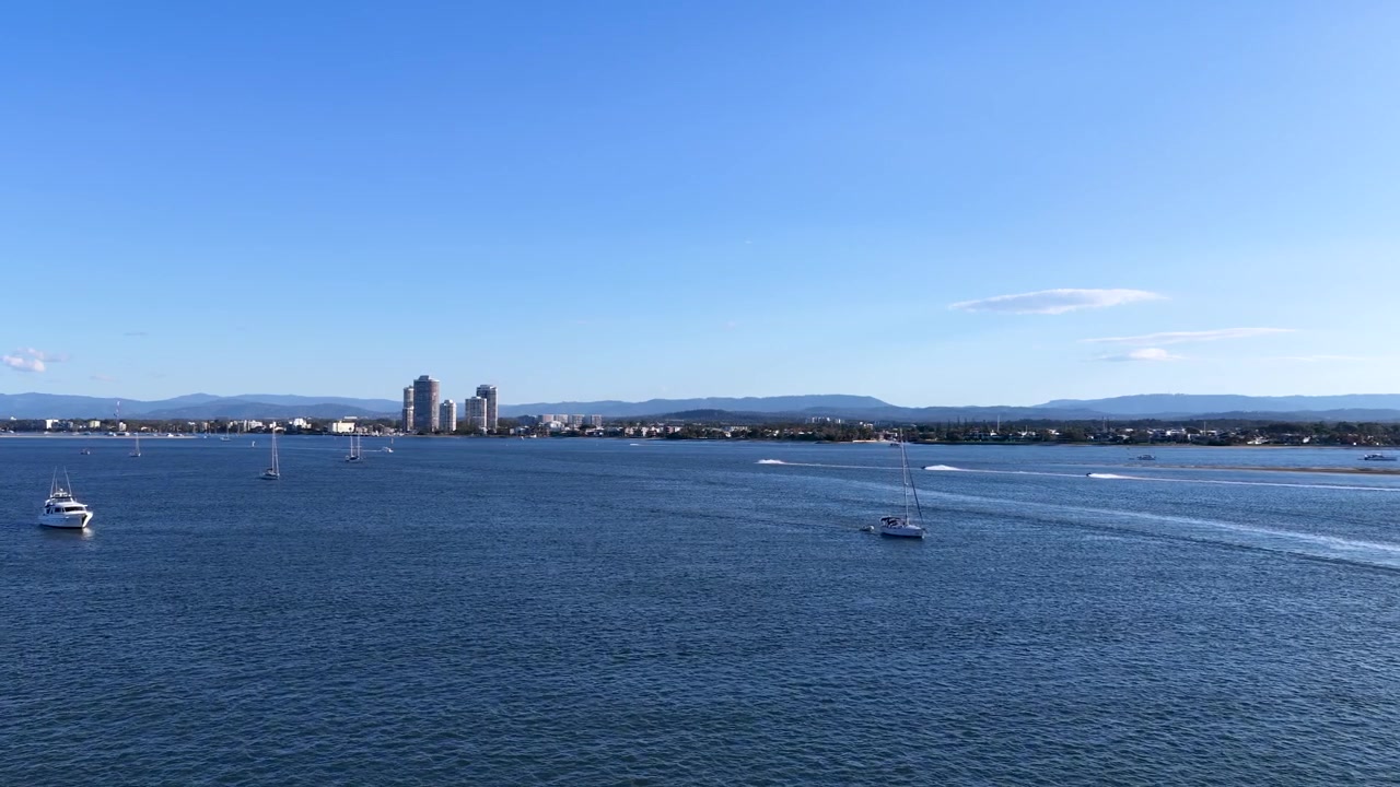 Ampia ripresa aerea di barche a vela sull'acqua blu con lo skyline della città a South Stradbroke